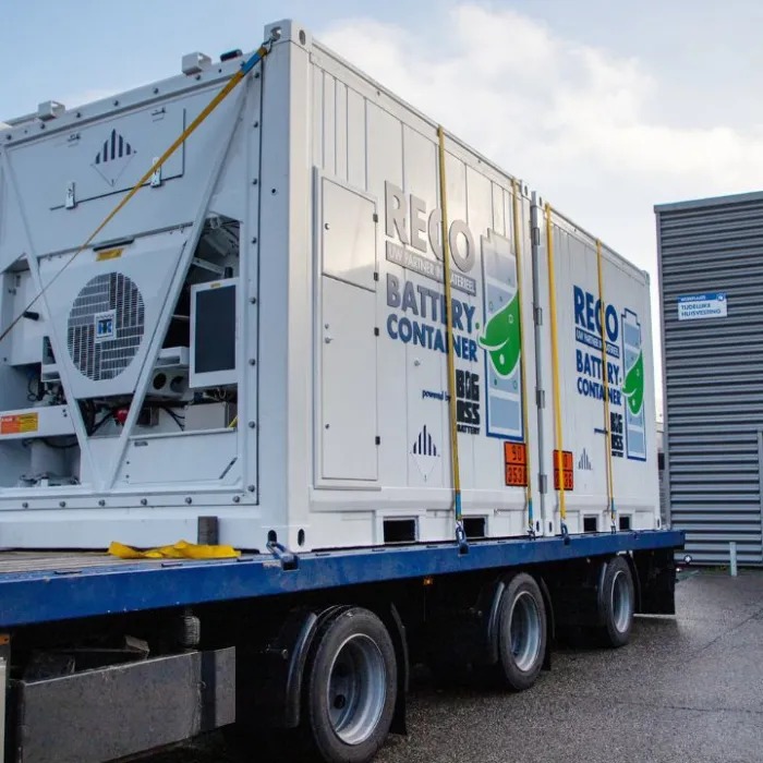 Twee batterijcontainers vastgesjord op een open oplegger, met oranje borden op de zijkant